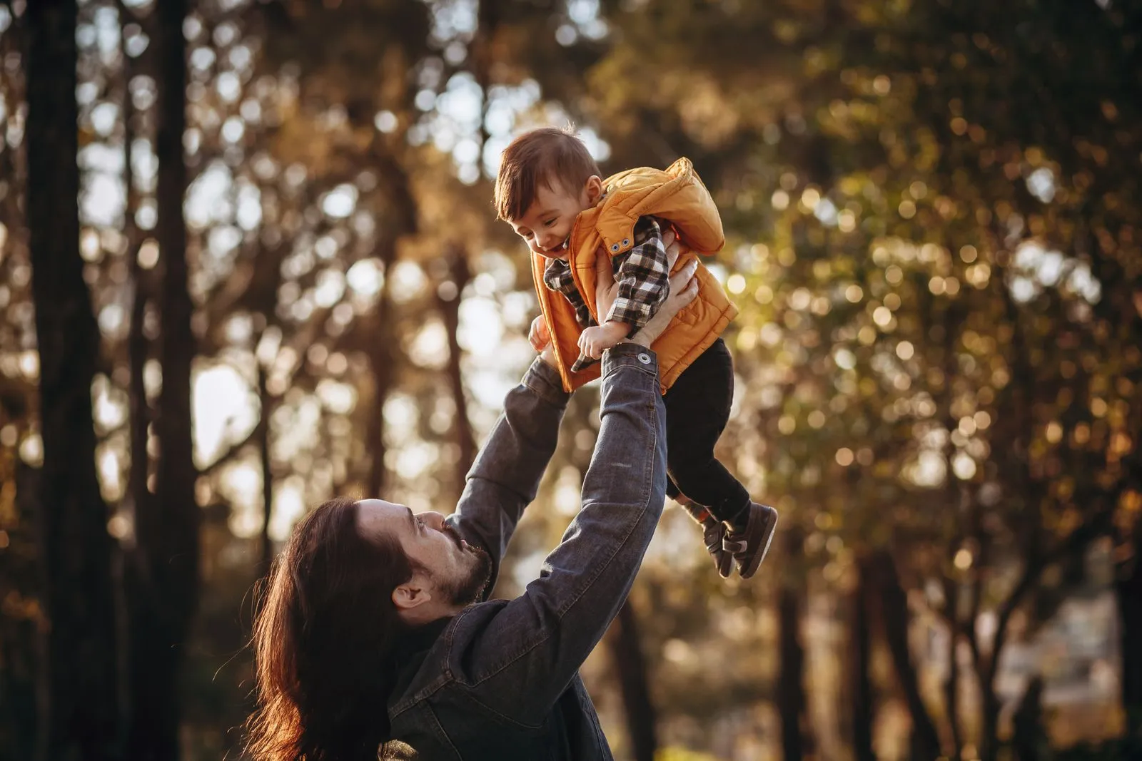 Father and son enjoying a playful moment in a sunlit park during autumn.